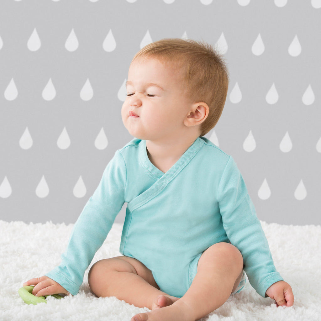 Infant sitting on a white carpet with their eyes closed wearing a blue organic baby kimono